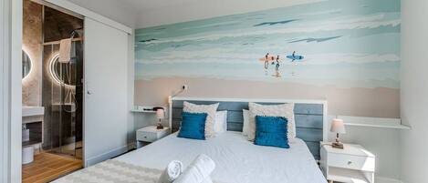 A hotel room with a large bed, a glass shower enclosure, and a beach mural on the wall.