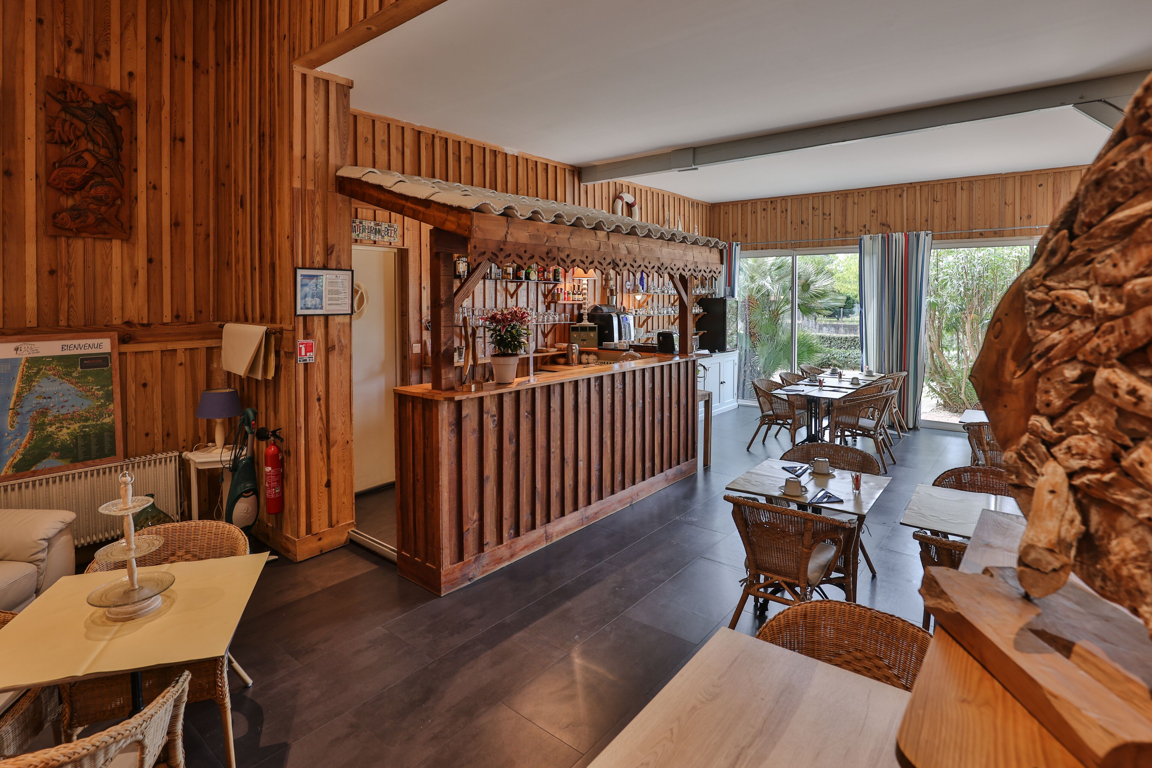 Un interior de madera con una zona de bar, mesas de comedor, muebles de mimbre y una gran escultura de madera.