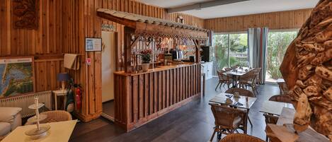 Un interior de madera con una zona de bar, mesas de comedor, muebles de mimbre y una gran escultura de madera.
