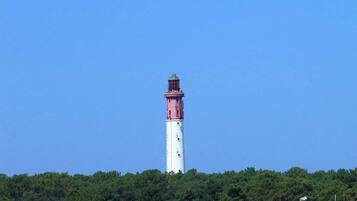Un faro con estructura blanca y roja, rodeado por una playa arenosa y vegetación escasa.