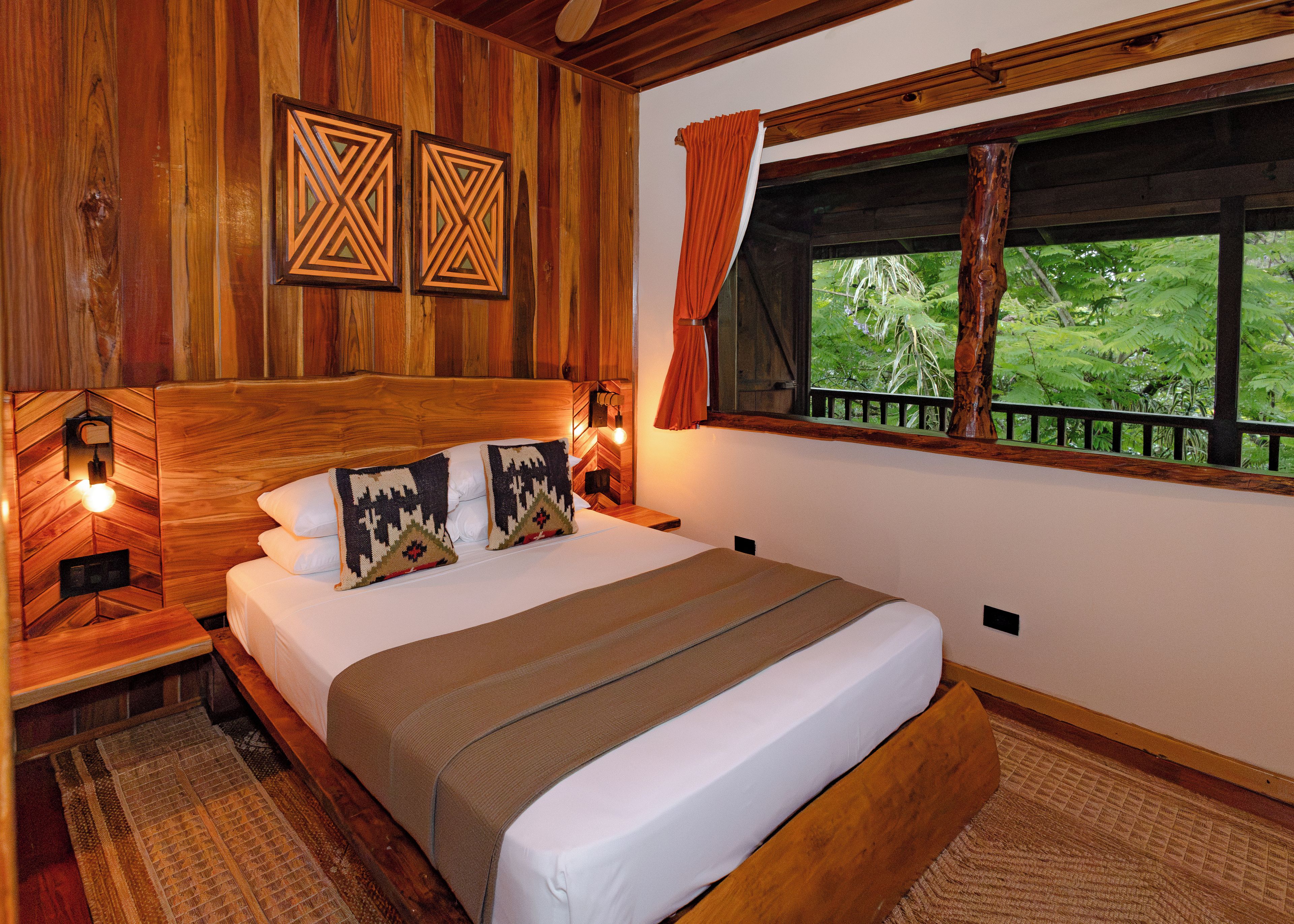 A wooden-themed bedroom with a bed, pillows, and a window with a view of greenery.