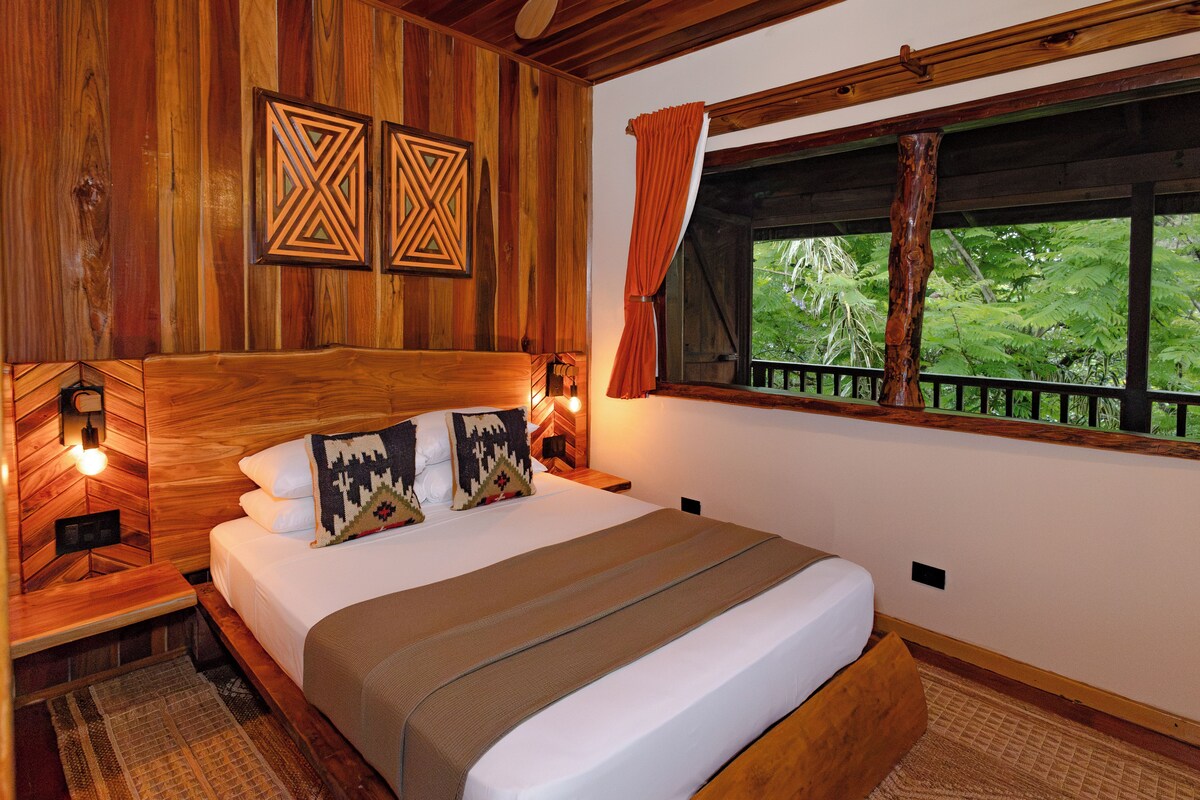 A wooden-themed bedroom with a bed, pillows, and a window with a view of greenery.