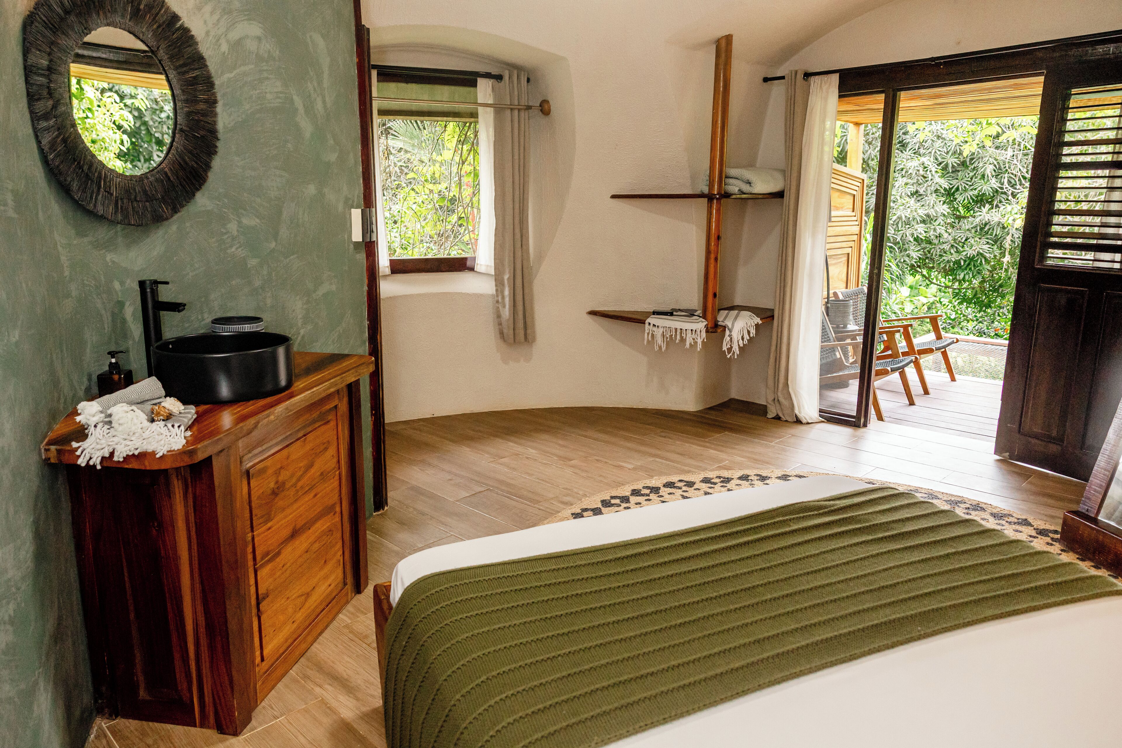 Un dormitorio con cómoda de madera, cama con manta verde, ventana con cortinas y vistas a zonas verdes.