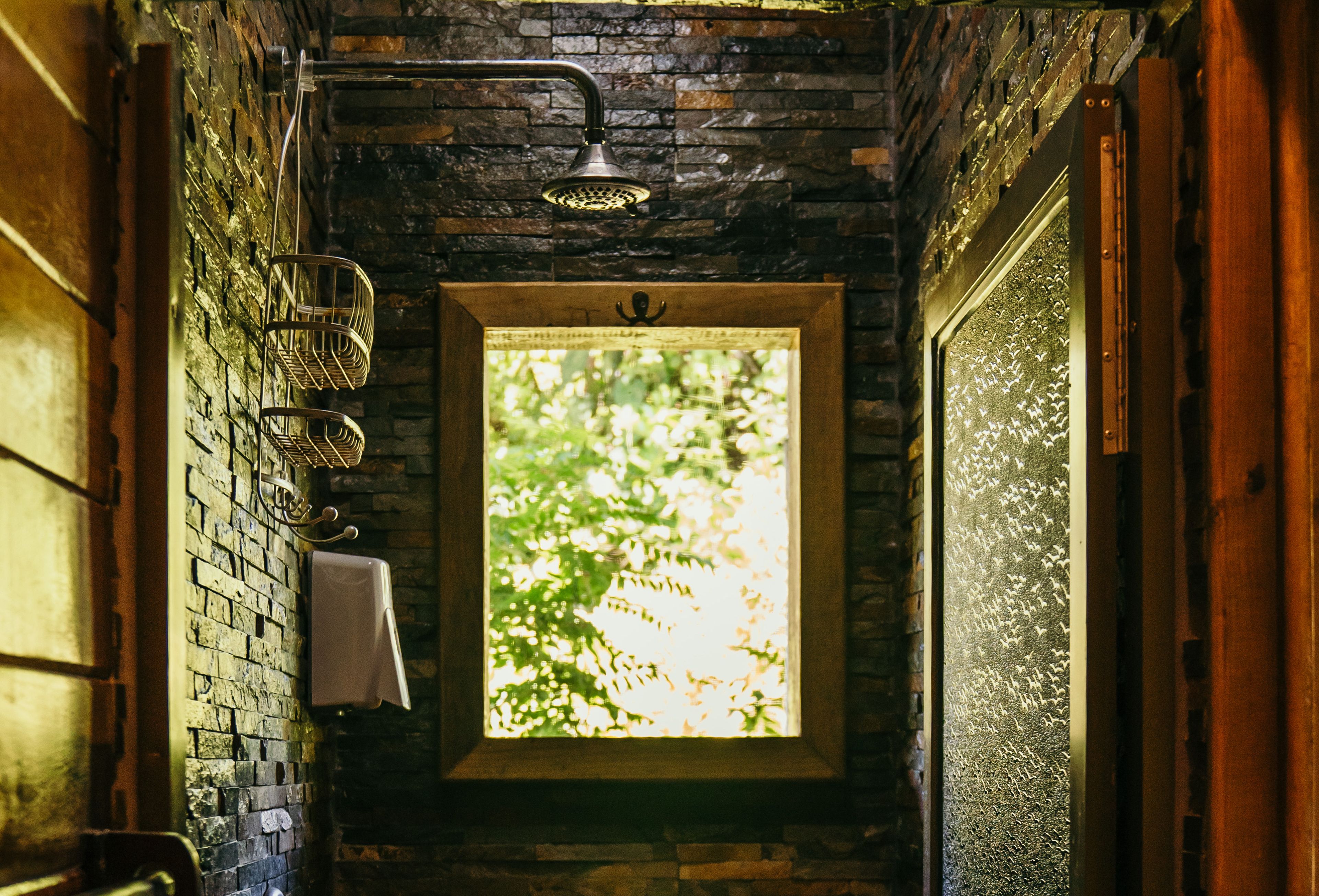 A narrow bathroom with a shower, a towel rack, and a window with a view of trees.