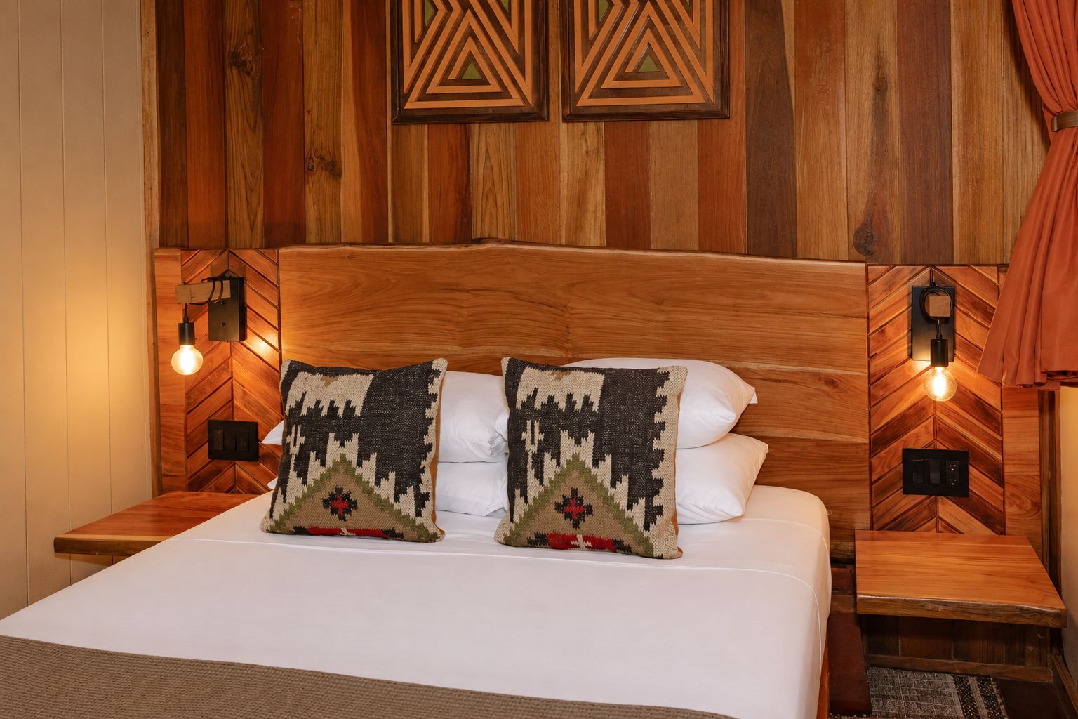Un lit avec deux coussins à motifs, une tête de lit en bois et deux appliques murales.