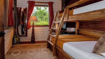 A cabin-style room with a bunk bed, a wooden ladder, a window with curtains, a lamp, and a rug.