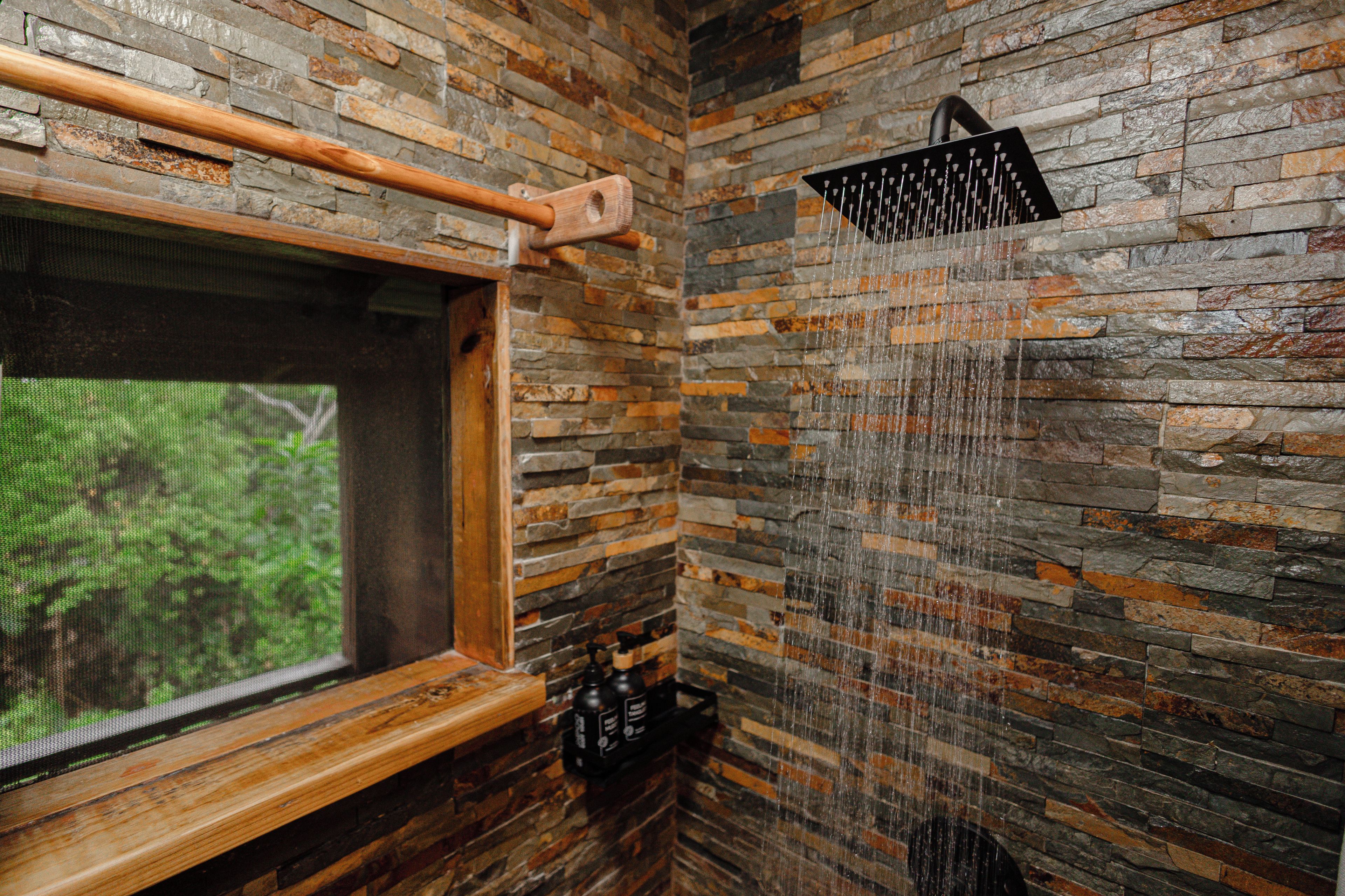 Una ducha con efecto de lluvia, un marco de ventana de madera y una pared de piedra.