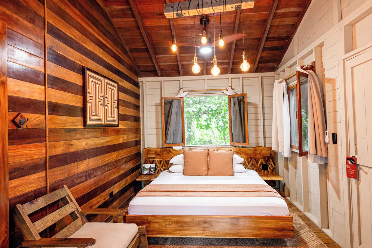 A wooden room with a bed, a chair, a window, and a door.