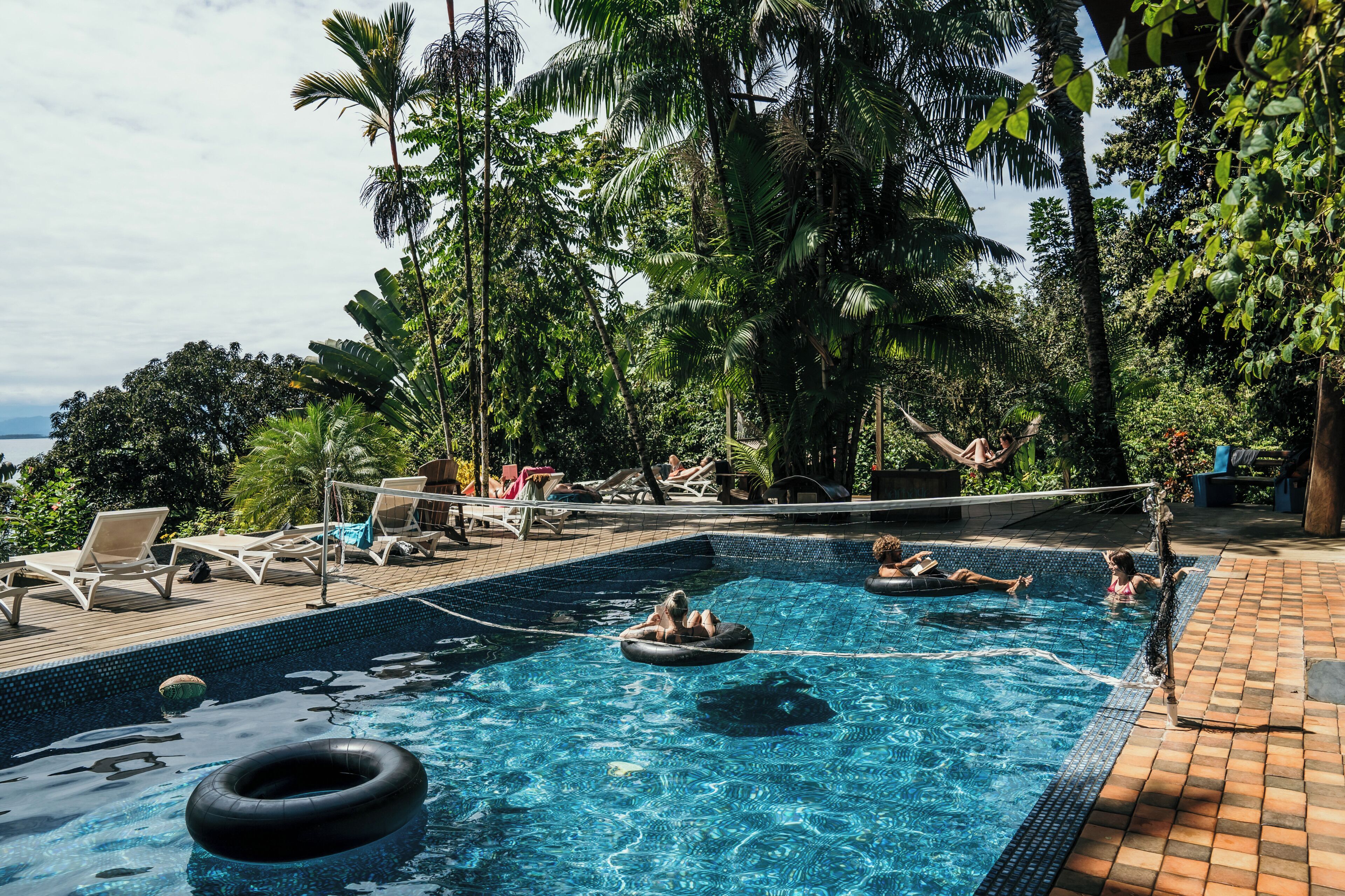 A swimming pool with lounge chairs and inflatable rings, surrounded by lush greenery.
