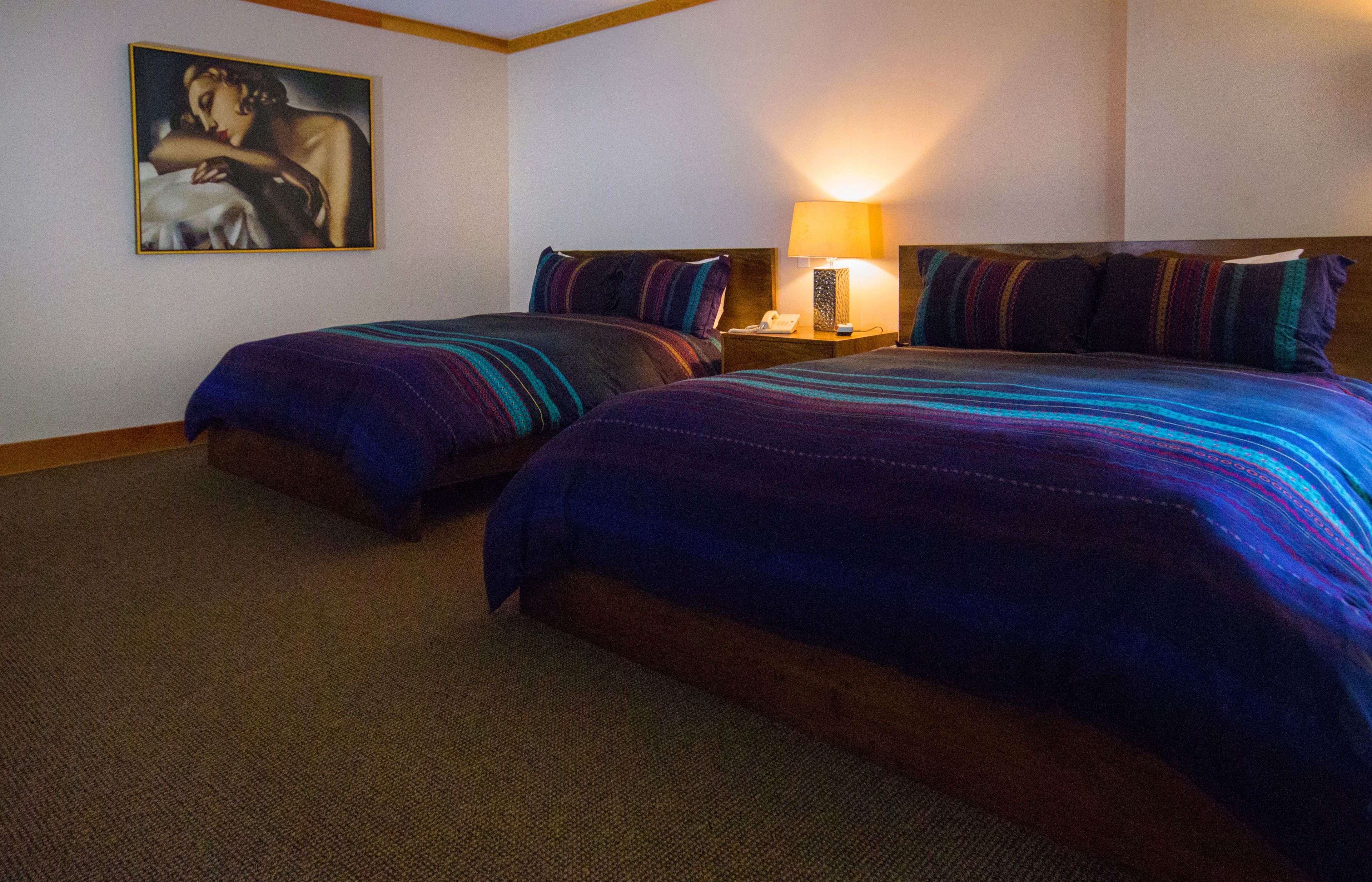 Een hotelkamer met twee bedden, een nachtkastje met een lamp en een schilderij aan de muur.