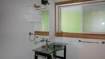 Un baño con lavamanos de vidrio, toallero, espejo y ventana con cristal esmerilado.