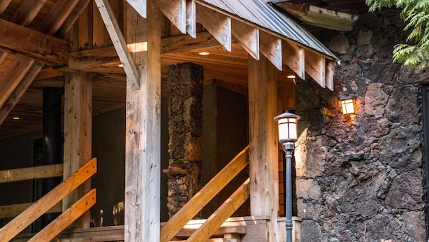 A wooden staircase leading to a stone building with a metal roof and a lantern on the wall.