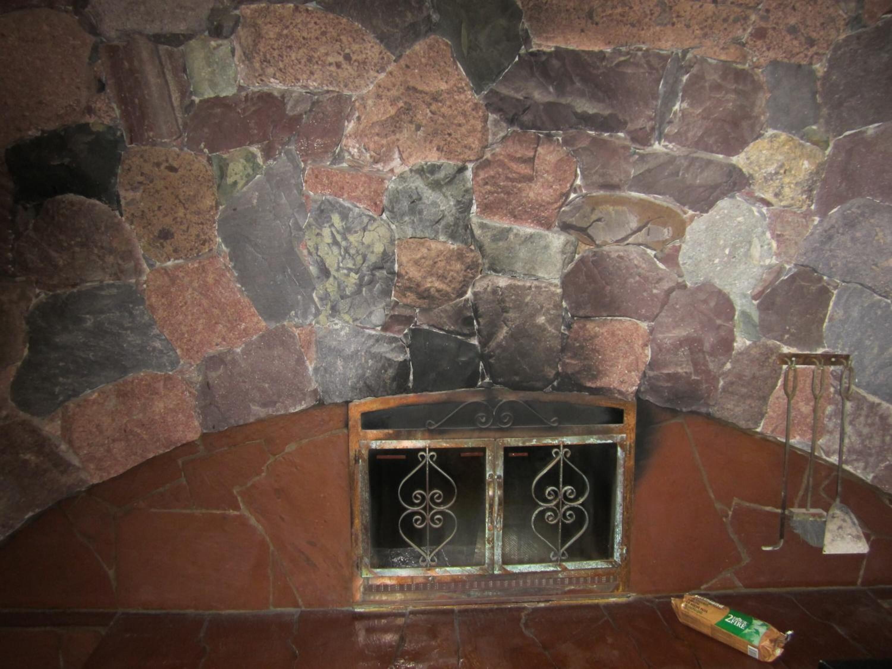 Eine Steinsäule mit Kamin, einem Metallgitter und einem Backsteinboden.