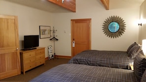A bedroom with two beds, a dresser, a television, a framed picture, a sunburst mirror, and a door with a lock.