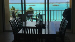 A dining area with a table and chairs, a glass, and a view of turquoise waters and islands.