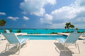 Zona junto a la piscina con sillones de descanso y vista al océano.