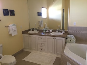 Un baño con dos lavamanos, un inodoro, una bañera y un espejo grande.