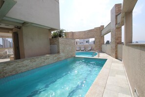 A rooftop swimming pool with clear blue water, surrounded by a brick wall and a tiled deck. - Caneca SP 101 (São Paulo)
