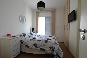 Un dormitorio con una cama, un aparador, un televisor y una puerta.