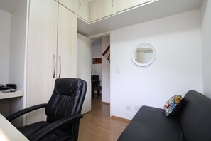 A compact living space with a black leather chair, a small round mirror, and a black sofa with a patterned pillow. - Caneca SP 101 (São Paulo)