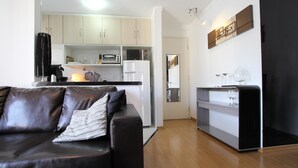 Een moderne woonkamer met een leren bank, een keuken met witte kastjes, een magnetron en een koelkast.