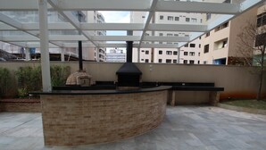 Een buitenkeuken van baksteen met een schoorsteen, omringd door een overdekt terras met glazen dak.