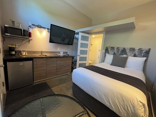 A compact hotel room with a bed, a small kitchenette, a TV, and a bathroom.