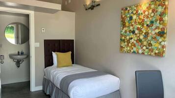 Une chambre à coucher comprenant un lit, une table de chevet, un miroir, un lavabo et un tableau abstrait aux couleurs vives accroché au mur.