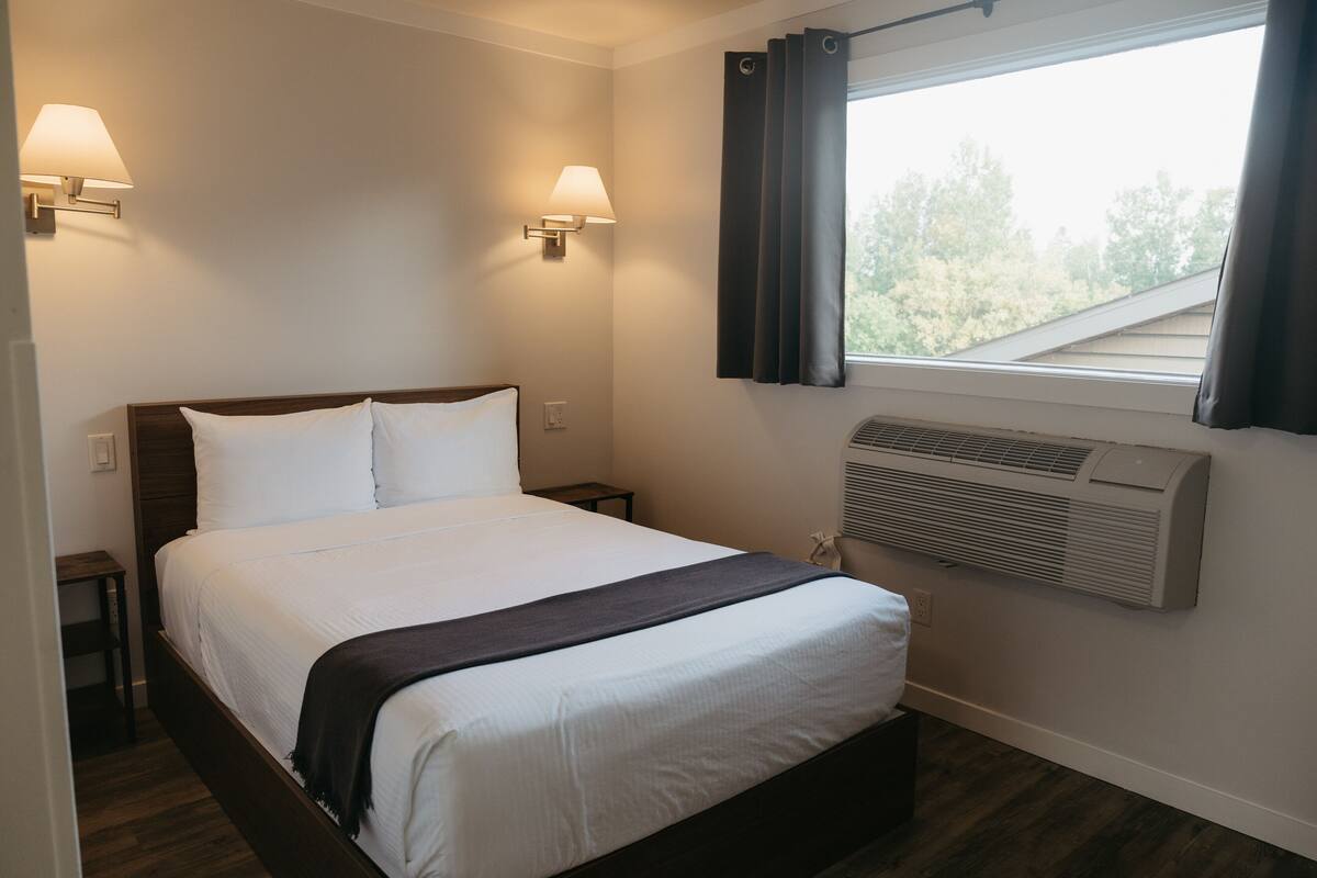 Une chambre d’hôtel comprenant un lit, deux lampes de chevet, une fenêtre avec des rideaux et un appareil de climatisation.