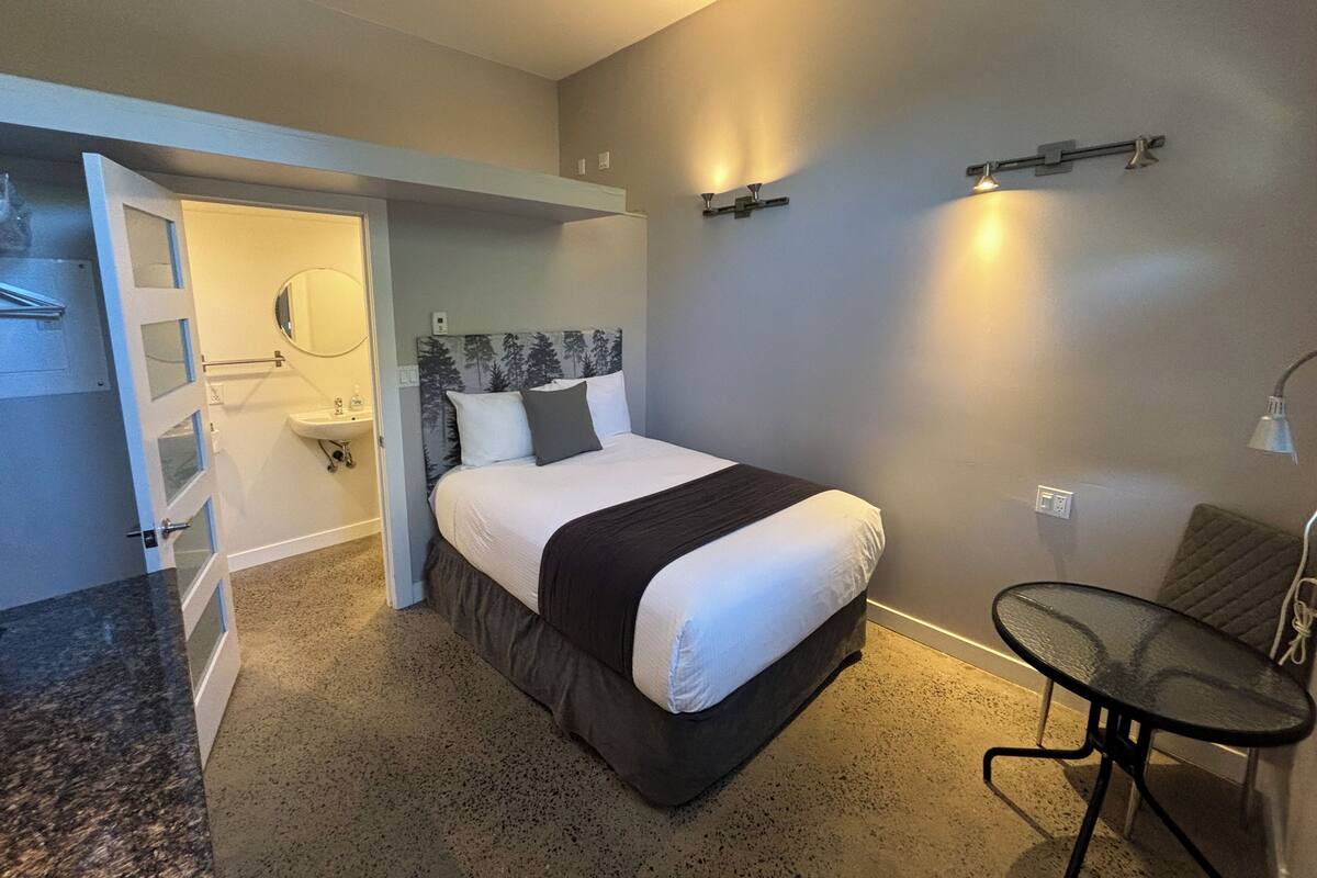Une chambre d’hôtel avec un lit, une petite table, une chaise, un lavabo et un miroir.