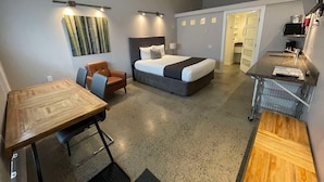 Une chambre d’hôtel de taille réduite, comprenant un lit, un bureau, une chaise et une kitchenette.