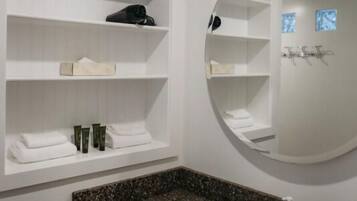 Une salle de bain dotée d’un comptoir en granit, d’un lavabo blanc et d’étagères où sont rangés les produits de toilette.