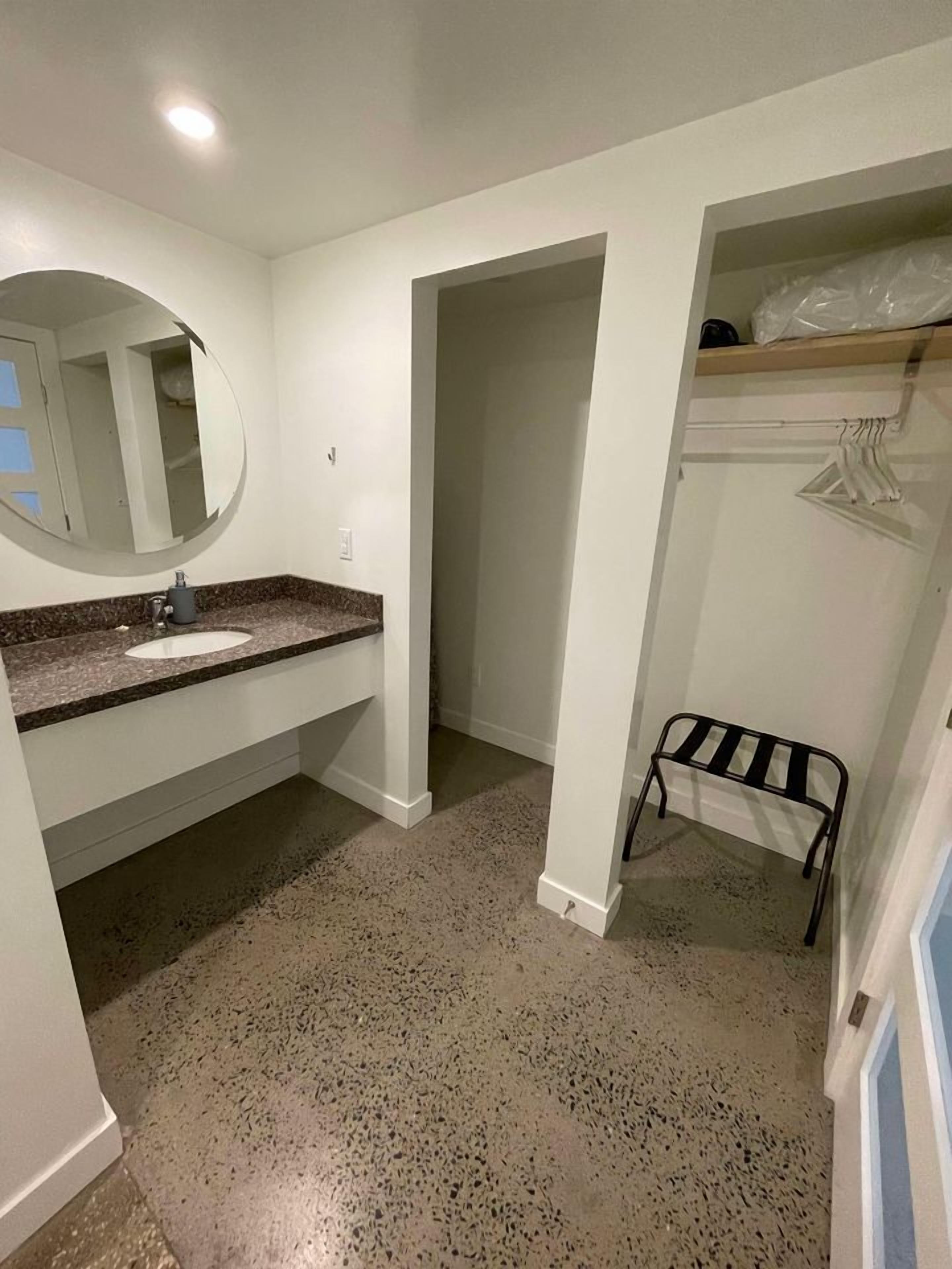 A bathroom with a white sink, a round mirror, and a speckled floor.
