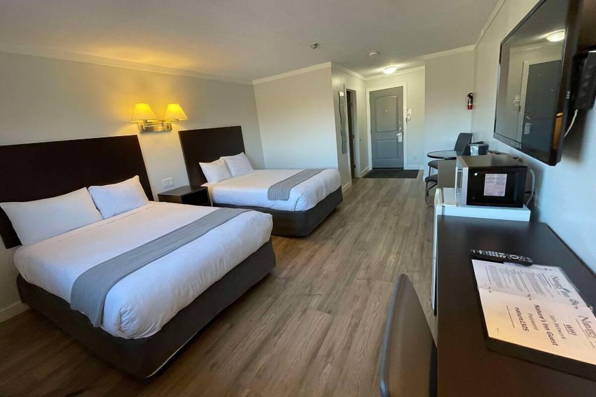 Une chambre d’hôtel avec deux lits, un bureau avec un ordinateur, une télévision et une porte donnant sur une salle de bain.