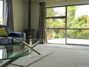Un salon avec une table basse en verre, un canapé, une cheminée et une grande porte-fenêtre coulissante donnant sur un jardin.
