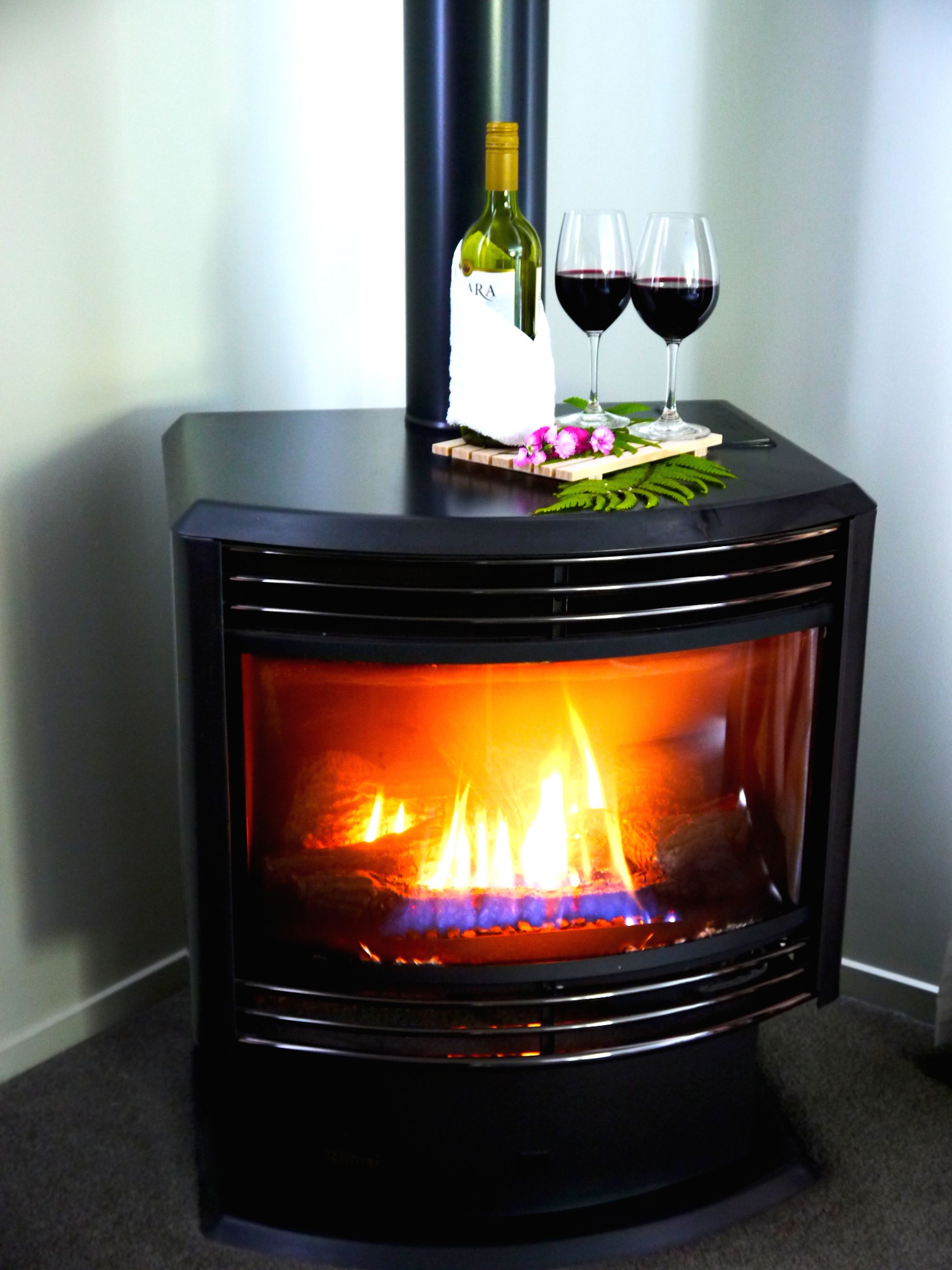 A wood-burning stove with a bottle of wine and two glasses on top.