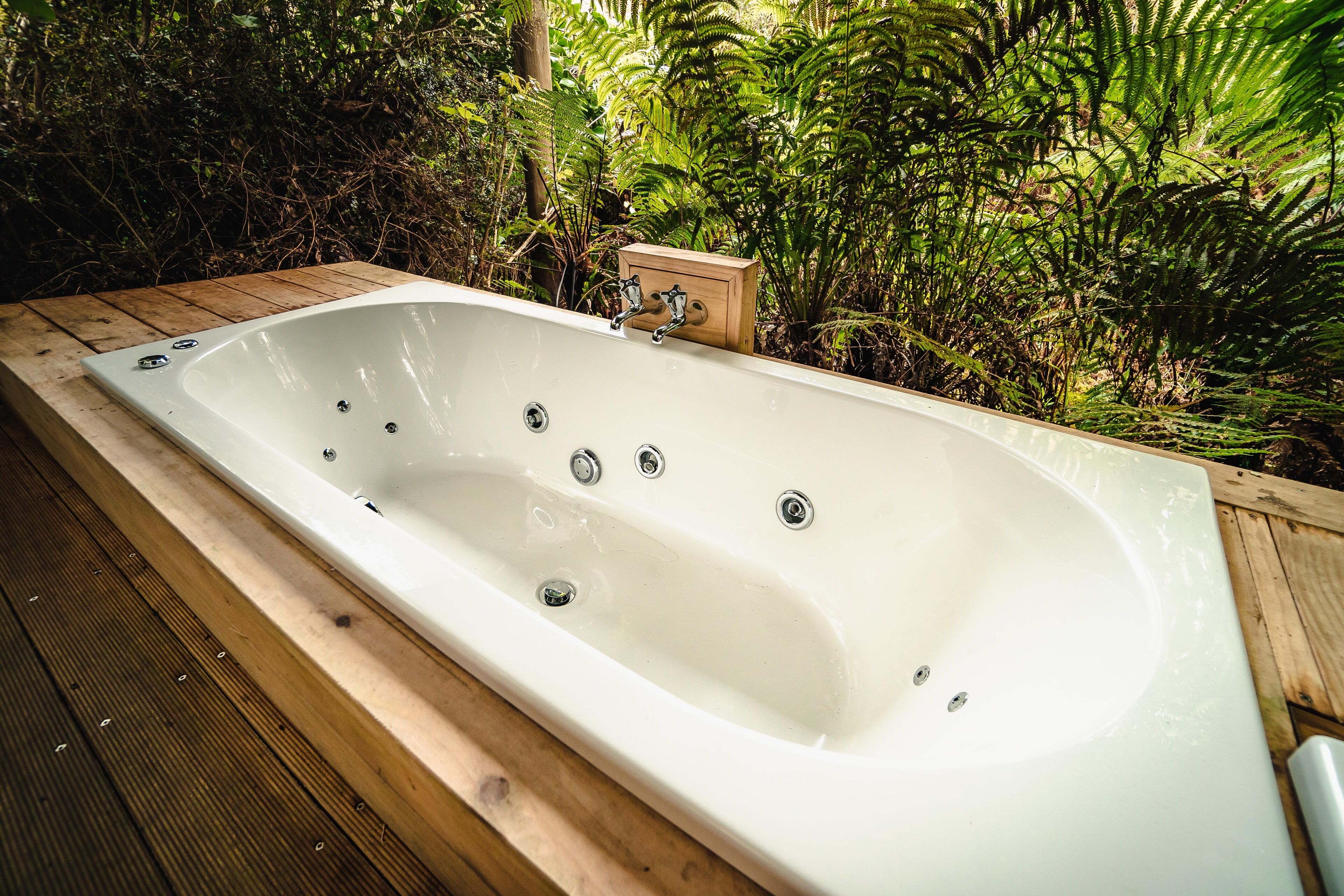 A rectangular hot tub with multiple faucets, surrounded by wooden decking and lush greenery.