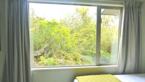 A room with a bed, a window with curtains, and a view of greenery outside.