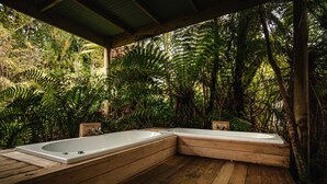 A wooden deck with two hot tubs surrounded by lush greenery.