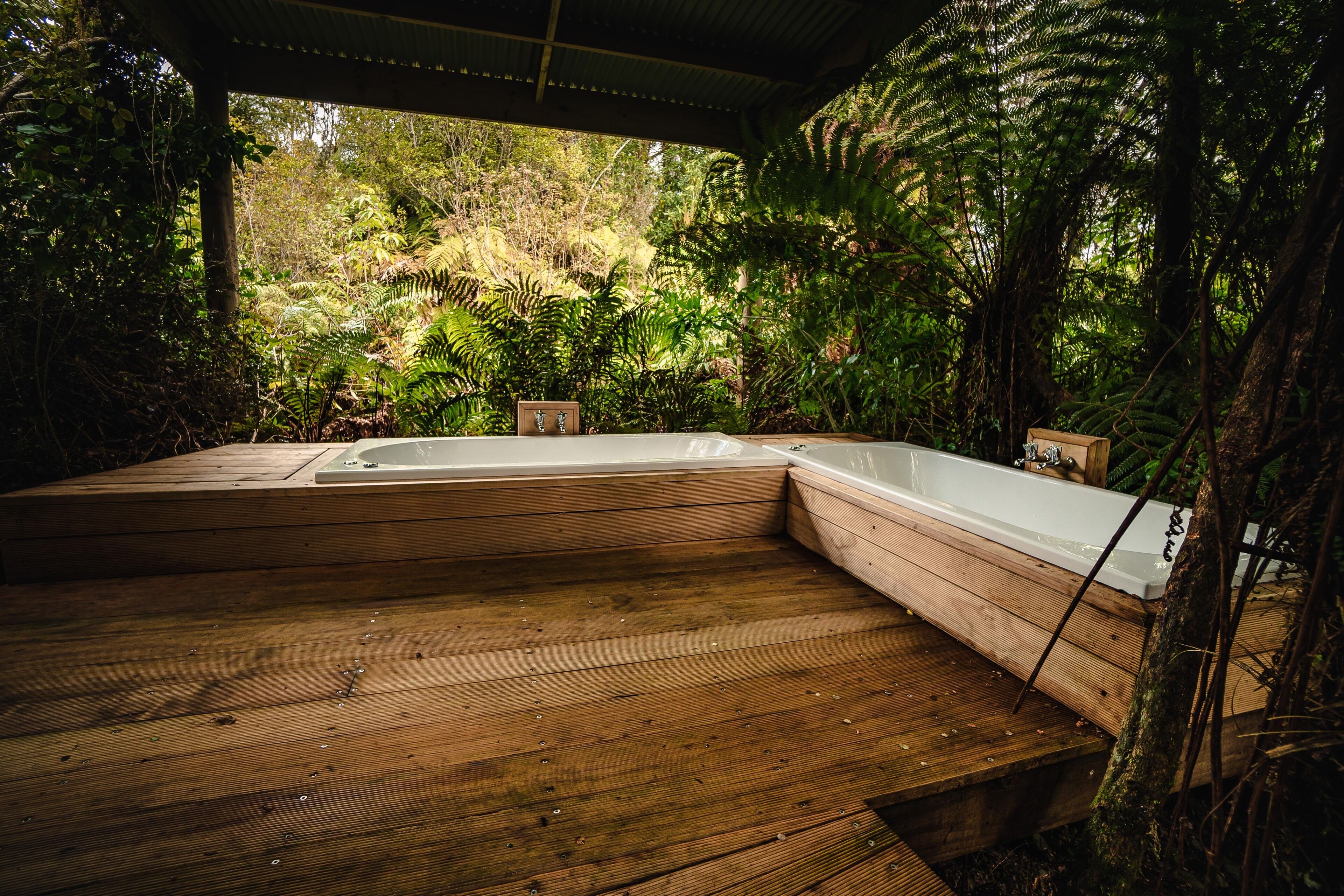 Una terraza de madera con un jacuzzi y un banco de madera, rodeada de abundante follaje.