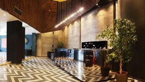 Un hall d’entrée moderne avec un sol décoré d’un motif en chevrons, un comptoir d’accueil et une grande plante en pot.