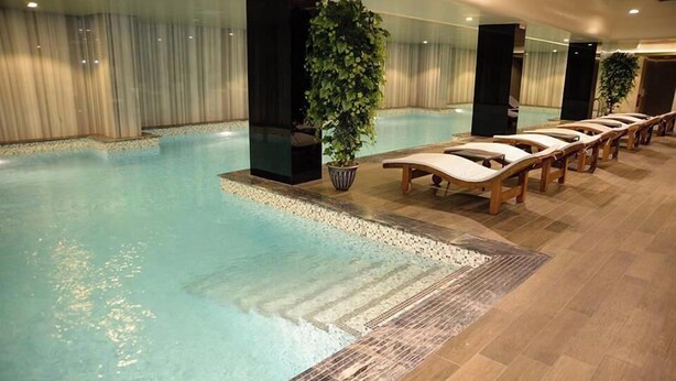 Une piscine intérieure dotée de chaises longues, d’une plante en pot et d’un sol carrelé.