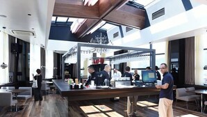 Un restaurant moderne doté d’un bar central, de planchers en bois et d’un plafond haut avec des puits de lumière.