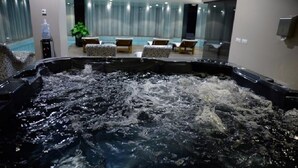 Un bain à remous où l’eau éclabousse, entouré de chaises longues et délimité par une paroi en verre.