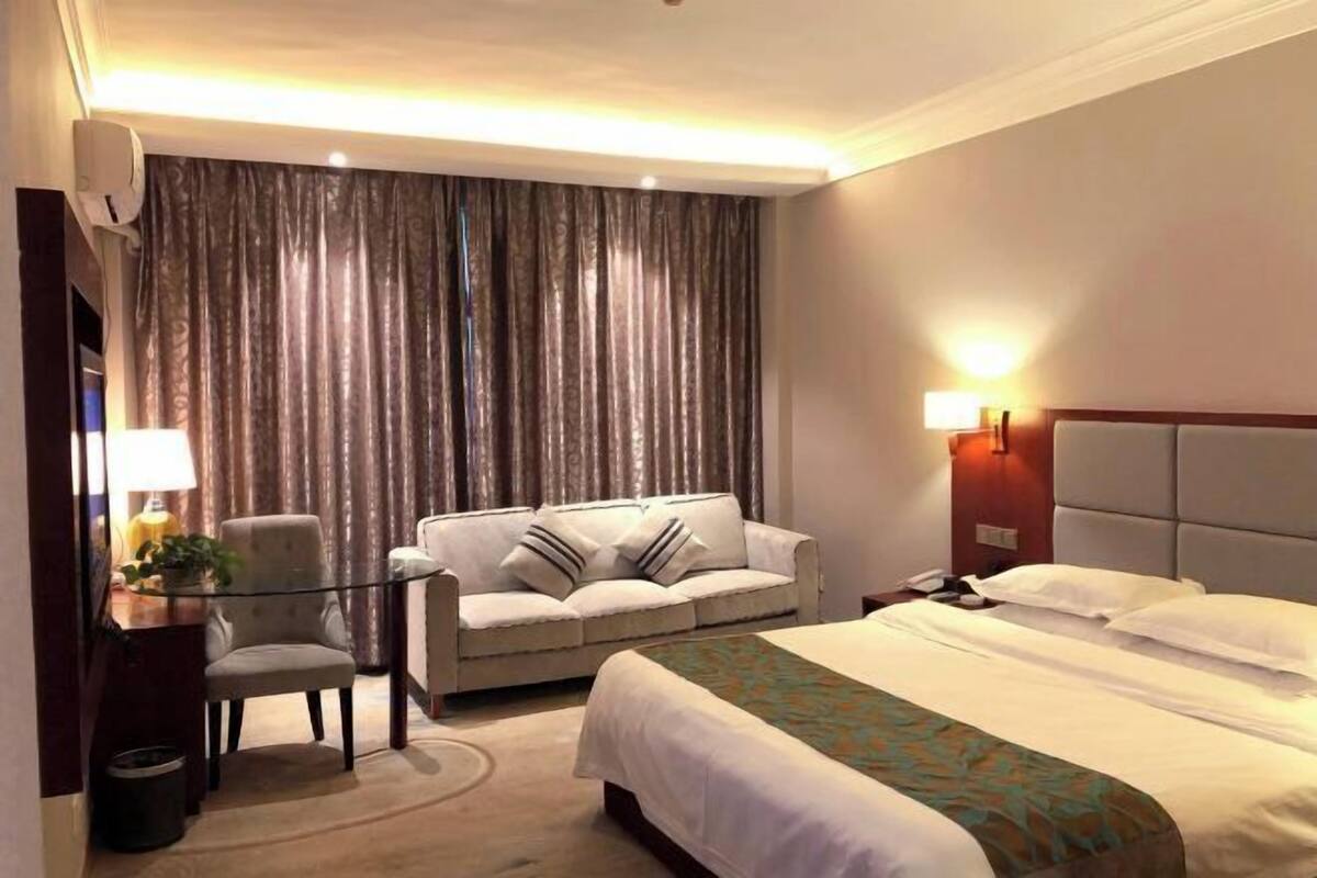 Une chambre d’hôtel avec un lit, un canapé, un bureau avec une lampe et un rideau.