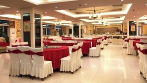 Un salón de banquetes con mesas redondas cubiertas con manteles rojos y sillas blancas adornadas con cintas rojas.