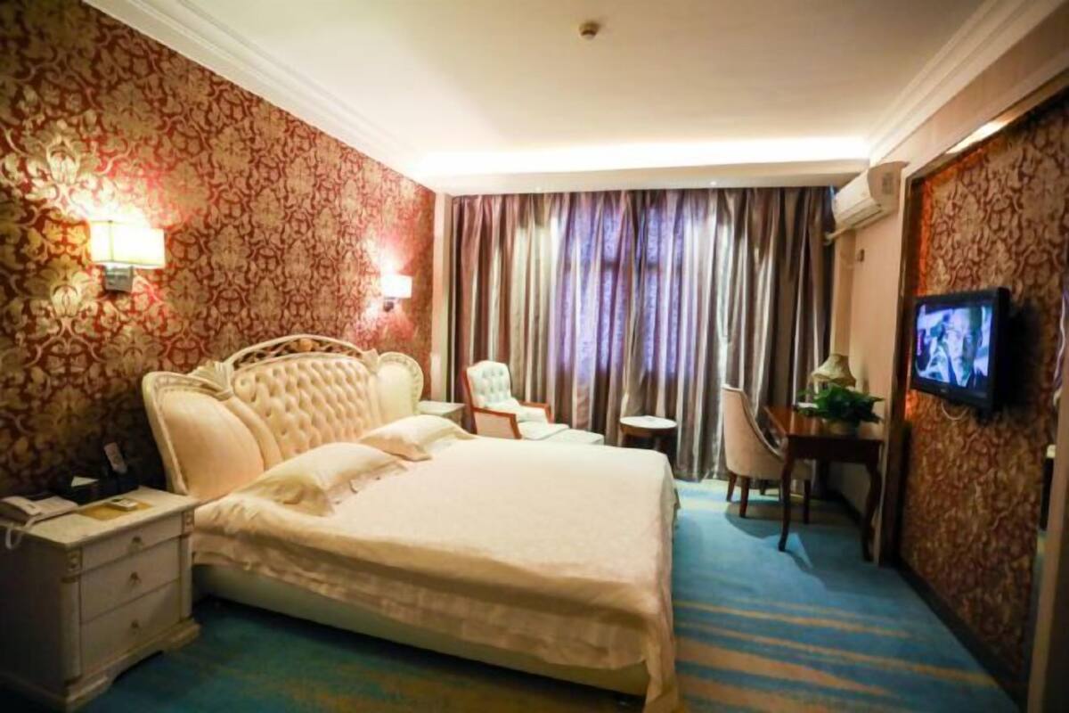 Une chambre d’hôtel avec un grand lit, un bureau, une chaise, une télévision et un papier peint à motifs.