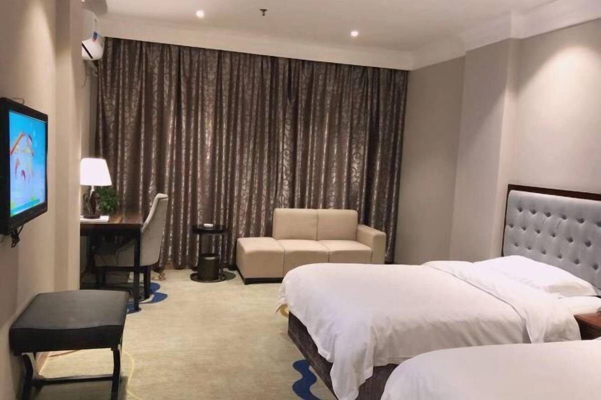 Une chambre d’hôtel avec deux lits, une télévision, un bureau, une chaise, un canapé et un rideau.
