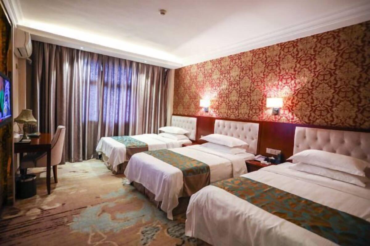 Une chambre d’hôtel avec deux lits, un bureau, une chaise, une télévision et un mur décoré de motifs.