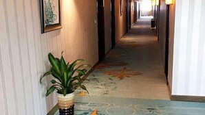 Pasillo de hotel con alfombra estampada, una planta en maceta y cuadros en las paredes.